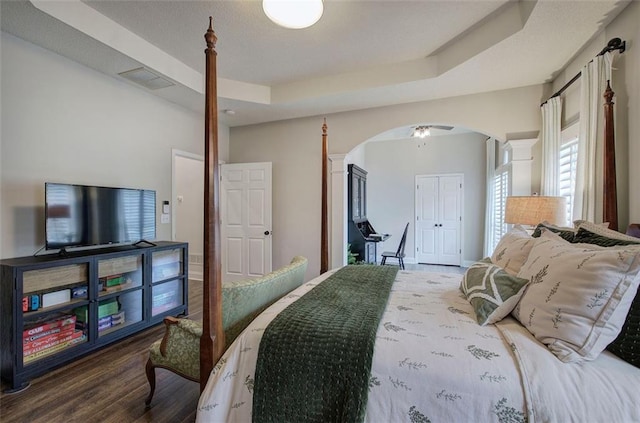 bedroom with arched walkways, visible vents, wood finished floors, and a raised ceiling