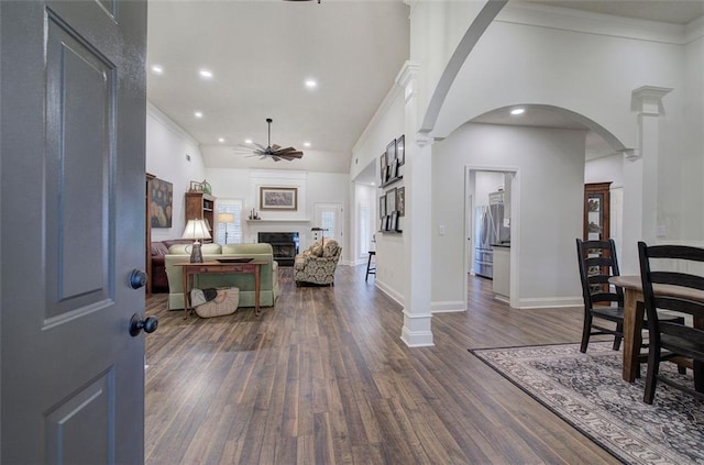 entryway featuring ceiling fan, arched walkways, a fireplace, dark wood-style floors, and ornate columns