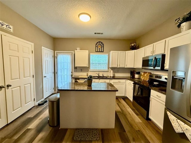 kitchen featuring appliances with stainless steel finishes, white cabinets, a textured ceiling, a kitchen island, and dark wood-style flooring