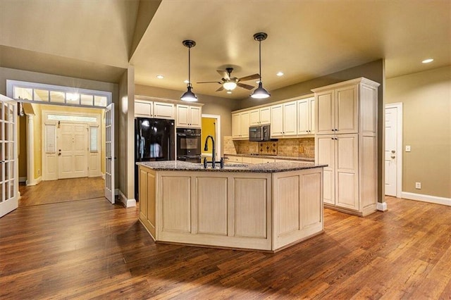 kitchen with decorative light fixtures, black appliances, sink, a kitchen island with sink, and dark stone counters