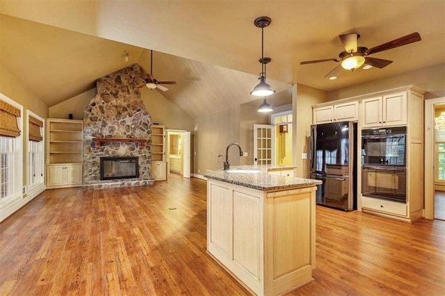 kitchen featuring black appliances, sink, hanging light fixtures, light stone countertops, and a stone fireplace