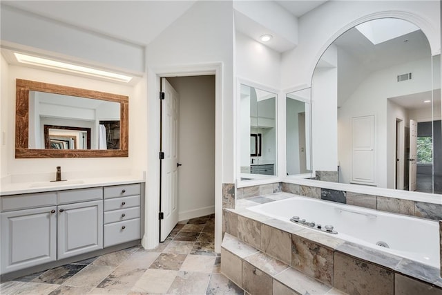 bathroom featuring vanity, lofted ceiling, and tiled tub