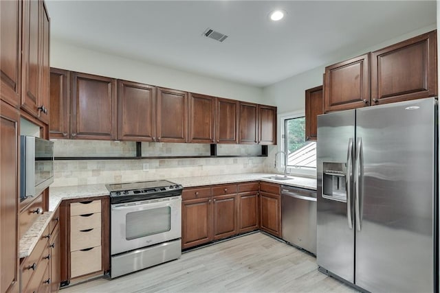 kitchen with light stone countertops, sink, stainless steel appliances, light hardwood / wood-style flooring, and decorative backsplash