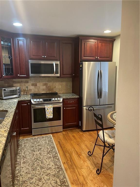 kitchen with stainless steel appliances, decorative backsplash, light hardwood / wood-style flooring, light stone counters, and sink