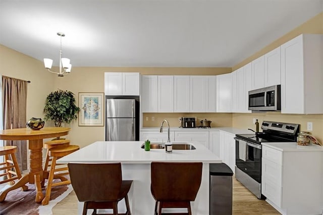 kitchen featuring pendant lighting, stainless steel appliances, an island with sink, and white cabinets