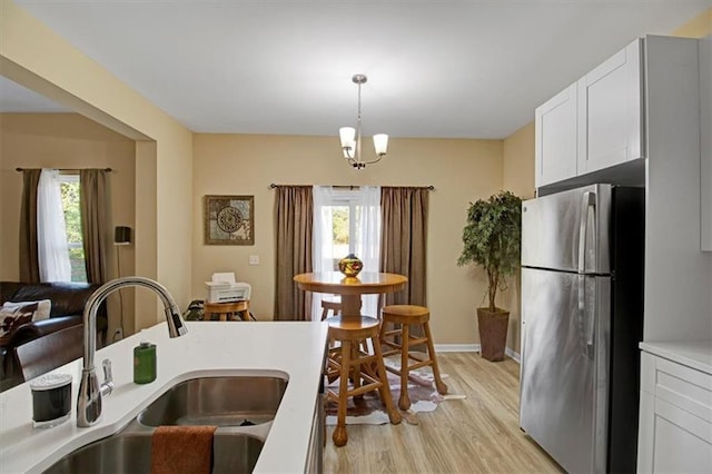 kitchen featuring stainless steel refrigerator, white cabinetry, sink, hanging light fixtures, and light wood-type flooring