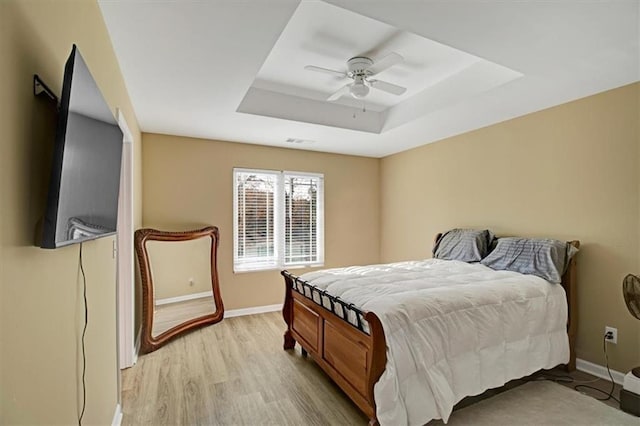 bedroom with ceiling fan, a tray ceiling, and light wood-type flooring