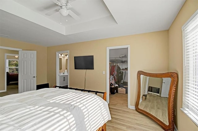 bedroom with a walk in closet, ensuite bath, light wood-type flooring, a tray ceiling, and a closet