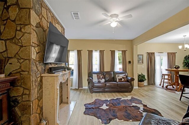 living room with ceiling fan with notable chandelier, a wealth of natural light, a high end fireplace, and light hardwood / wood-style floors