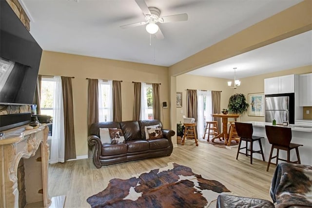 living room with ceiling fan with notable chandelier and light hardwood / wood-style floors