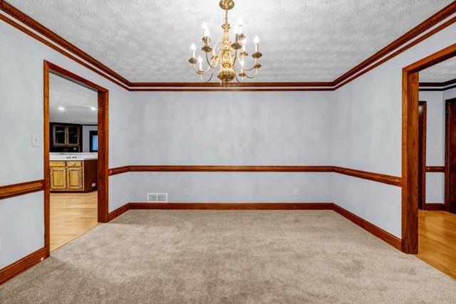 362 Clyde Ct, Mcdonough, GA 30252 - spare room featuring ornamental molding, a chandelier, light carpet, a textured ceiling, and baseboards