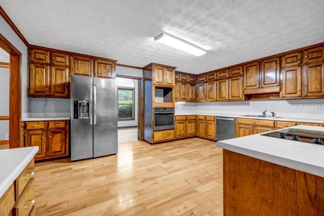362 Clyde Ct, Mcdonough, GA 30252 - kitchen with appliances with stainless steel finishes, light wood-type flooring, a textured ceiling, brown cabinetry, and light countertops