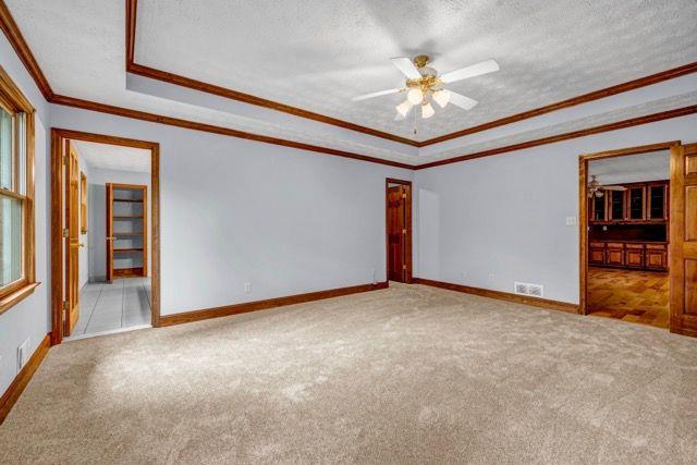 362 Clyde Ct, Mcdonough, GA 30252 - carpeted empty room with a ceiling fan, baseboards, a tray ceiling, a textured ceiling, and crown molding