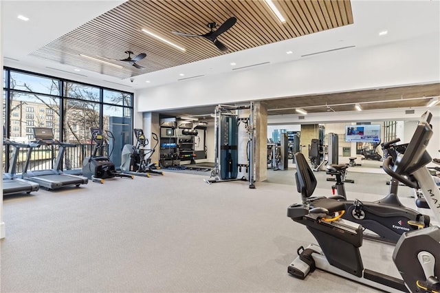 gym featuring a tray ceiling, ceiling fan, light carpet, floor to ceiling windows, and wooden ceiling