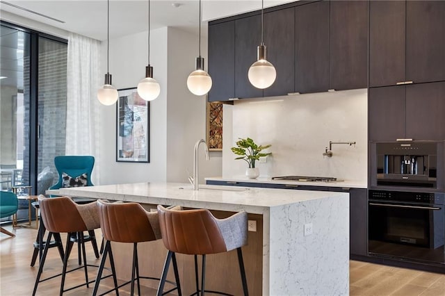 kitchen featuring light stone countertops, light hardwood / wood-style floors, a center island with sink, and a breakfast bar area