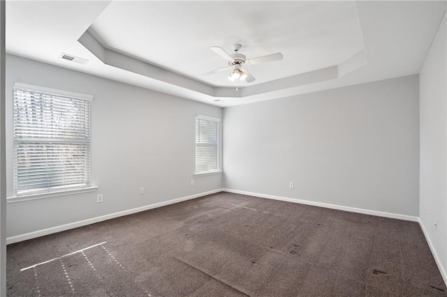 empty room featuring ceiling fan, a raised ceiling, and dark colored carpet