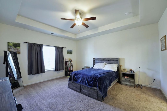 carpeted bedroom featuring ceiling fan and a raised ceiling