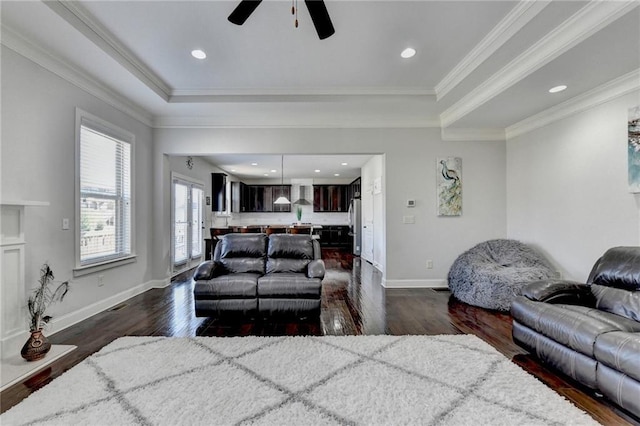 living room featuring baseboards, ornamental molding, dark wood-type flooring, a tray ceiling, and ceiling fan