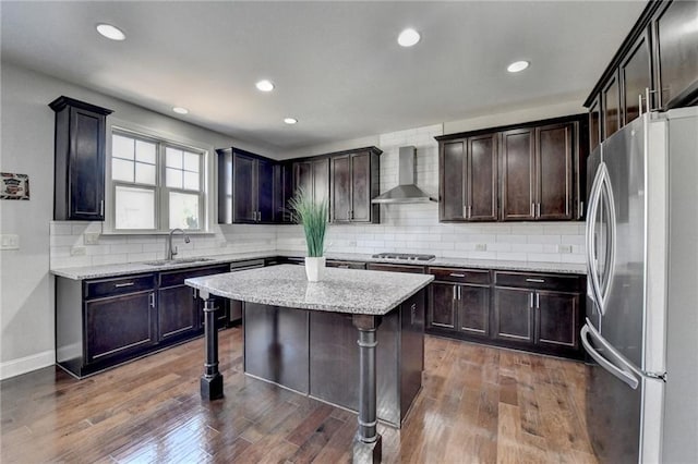 kitchen with a sink, appliances with stainless steel finishes, wall chimney exhaust hood, and dark wood finished floors