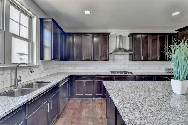 kitchen featuring wall chimney exhaust hood, dark wood-type flooring, appliances with stainless steel finishes, light stone counters, and a sink