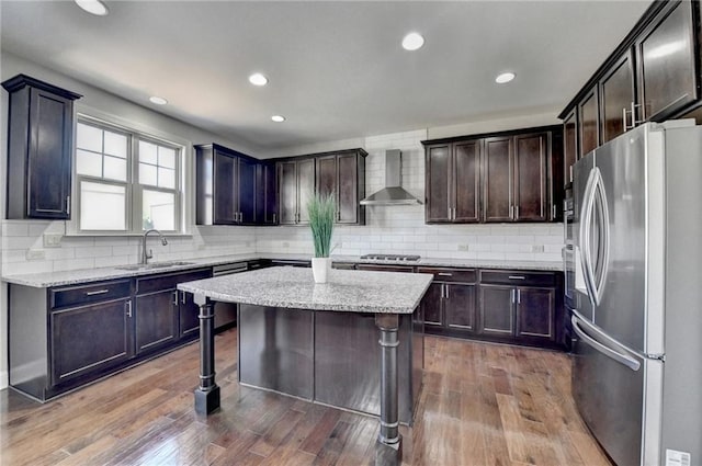 kitchen with stainless steel appliances, tasteful backsplash, a sink, and wall chimney range hood