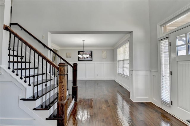 foyer featuring crown molding, a wealth of natural light, an inviting chandelier, and dark wood-style floors