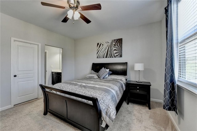 bedroom with ensuite bathroom, light colored carpet, baseboards, and ceiling fan