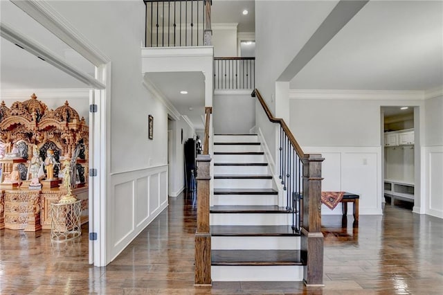staircase with crown molding, a decorative wall, and wood finished floors