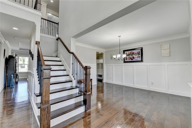 stairs with an inviting chandelier, a decorative wall, ornamental molding, and wood finished floors