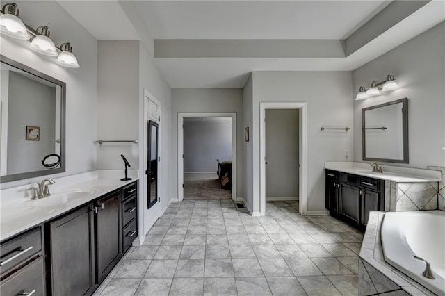 bathroom featuring a sink, two vanities, tiled tub, and baseboards