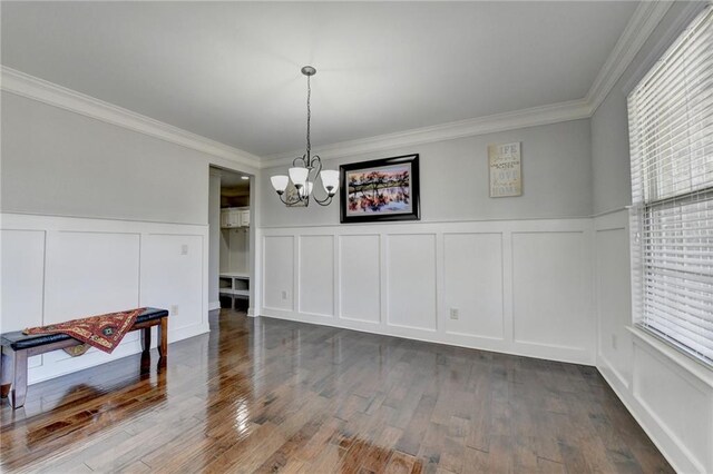 unfurnished dining area with a decorative wall, ornamental molding, a chandelier, and dark wood-style flooring