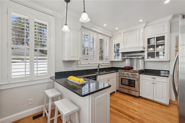 kitchen featuring light wood finished floors, appliances with stainless steel finishes, a peninsula, white cabinetry, and a sink