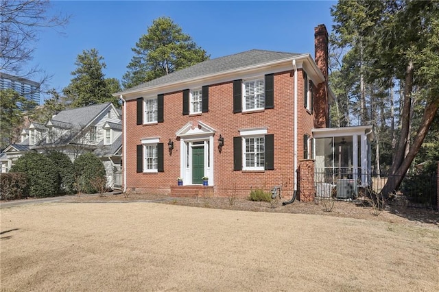 colonial-style house with cooling unit, a sunroom, brick siding, and a chimney