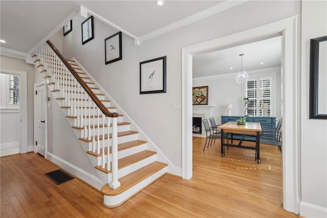 stairs featuring baseboards, wood finished floors, visible vents, and crown molding