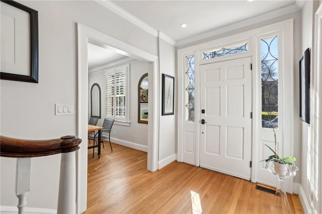 foyer with light wood-type flooring, baseboards, visible vents, and crown molding