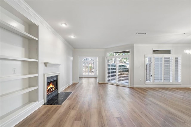 unfurnished living room featuring built in shelves, light wood-type flooring, a warm lit fireplace, and baseboards