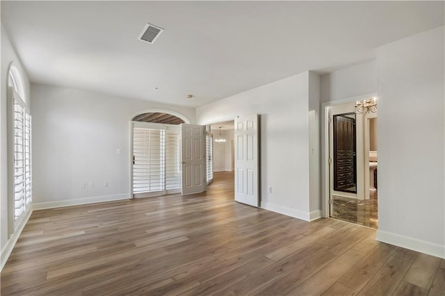 unfurnished bedroom featuring baseboards, visible vents, a notable chandelier, and wood finished floors