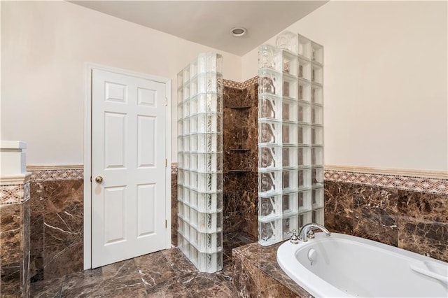 full bath with wainscoting, a bath, marble finish floor, a walk in shower, and tile walls