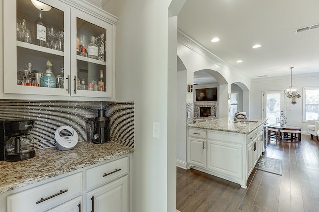 kitchen with light stone counters, glass insert cabinets, white cabinetry, dark wood-style floors, and decorative light fixtures