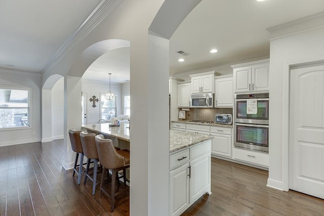 kitchen featuring light stone counters, appliances with stainless steel finishes, white cabinets, and arched walkways