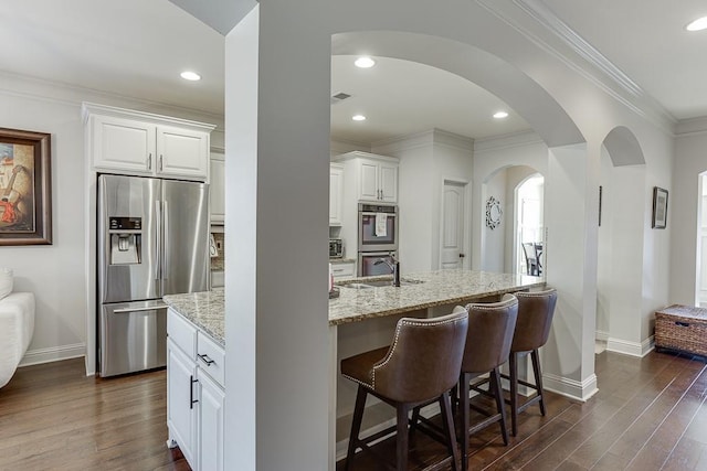 kitchen with dark wood finished floors, light stone counters, stainless steel appliances, white cabinetry, and a sink