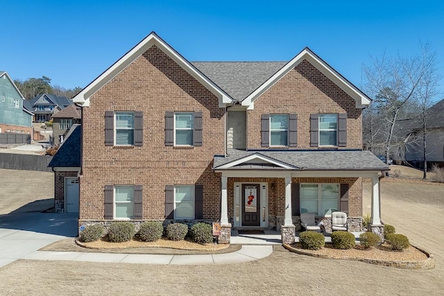 view of front of property featuring covered porch, brick siding, driveway, and roof with shingles