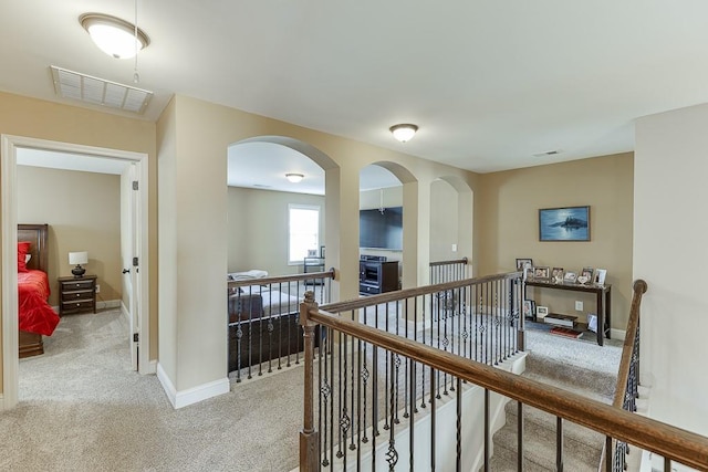 hallway featuring light carpet, an upstairs landing, visible vents, and baseboards