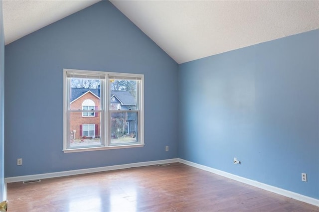 unfurnished room with visible vents, vaulted ceiling, baseboards, and wood finished floors