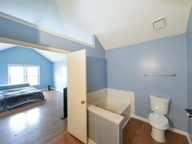 bathroom featuring lofted ceiling, tile patterned flooring, a garden tub, and toilet