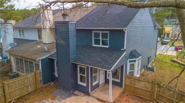 back of property featuring a shingled roof, a chimney, a patio area, and fence