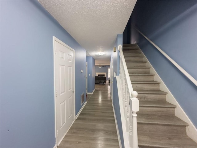 staircase featuring a textured ceiling, wood finished floors, visible vents, and baseboards