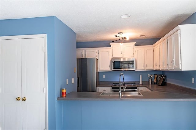 kitchen with a textured ceiling, a peninsula, a sink, white cabinets, and appliances with stainless steel finishes