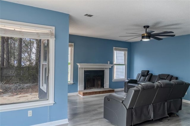 living room featuring a brick fireplace, wood finished floors, visible vents, and baseboards