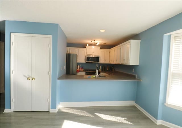 kitchen with light wood-type flooring, kitchen peninsula, stainless steel appliances, and white cabinetry